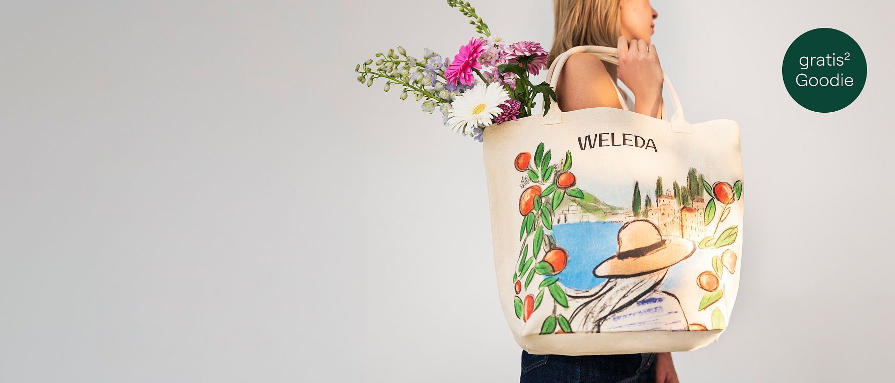 Frau hält mit Blumen gefüllte Tasche in der Hand. Auf der Tasche ist ein maritimites Design sowie das Weleda-Logo abgebildet.