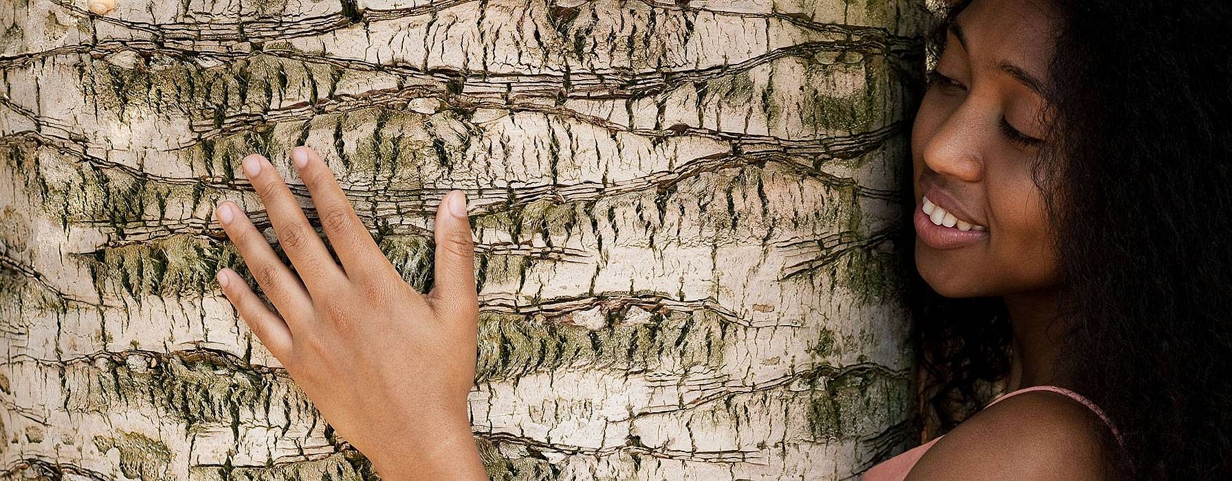 Lächelnde Frau umarmt einen Baum