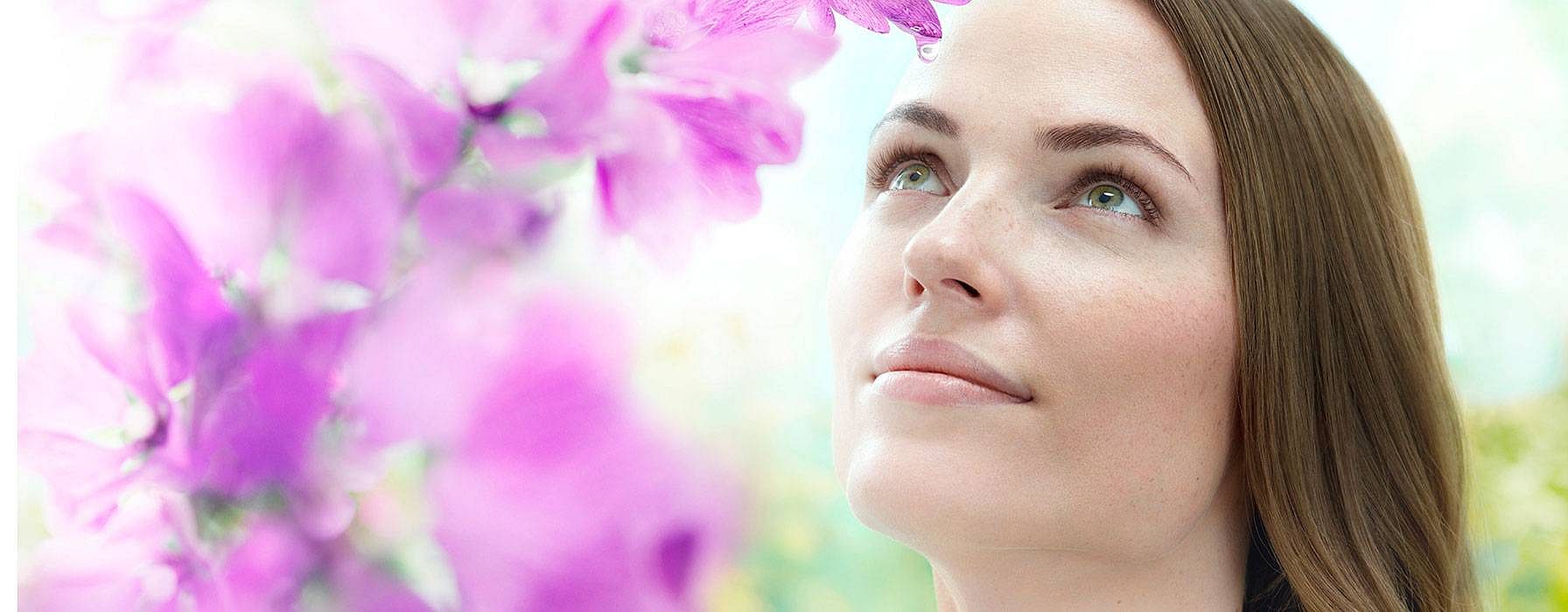 Frau mit Malvenblüten im Hintergrund schaut in den Himmel