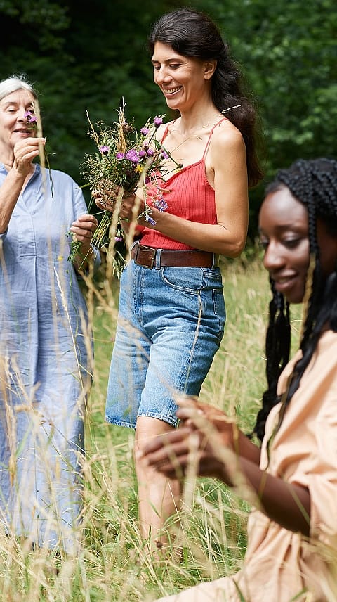 Drei Frauen unterschiedlichen Alters pfluecken gemeinsam Blumen auf einer Wiese
