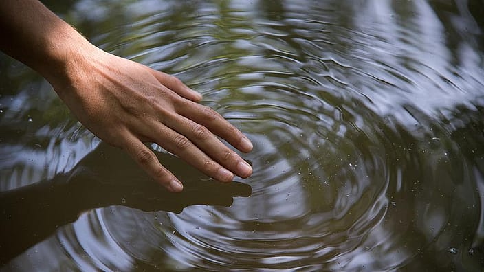 Hand beruehrt Wasseroberflaeche, Wasser zieht Kreise