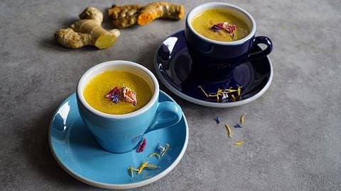 zwei blaue Tassen mit veganer Moonmilk, in Hintergrund liegt eine gelbe Kurkumawurzel