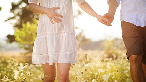 Schwangere Frau spaziert in der Natur mit einem Mann an der Hand