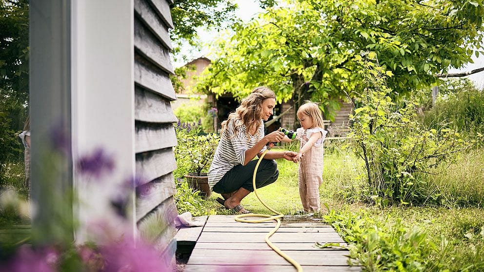 Frau lindert Stich  mit Gartenschlauch