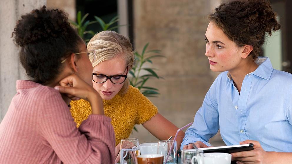 3 junge Frau am Tisch mit Getränken besprechen sich