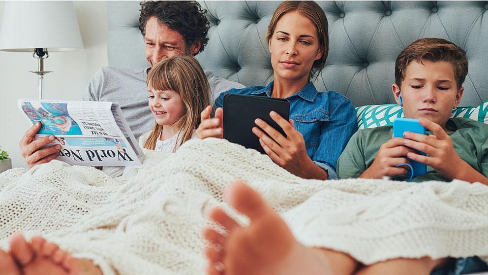 Familie im Bett mit digitalen Geräten